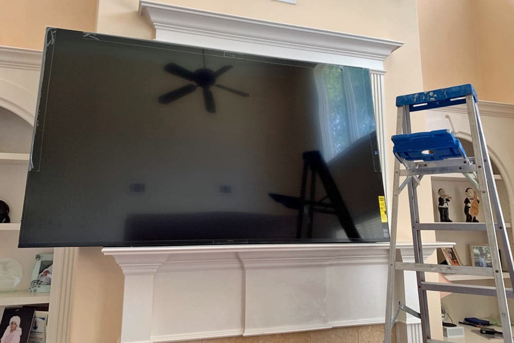 huge tv being mounted above fireplace mantle with ladder by professional handyman in desoto county mississippi.