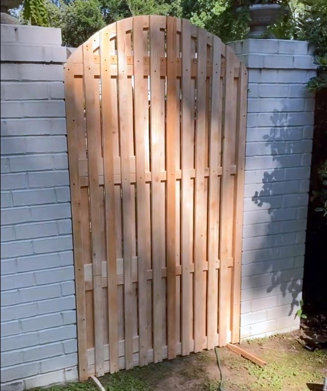 mounting a new wooden gate in the opening of two white brick pillars in the backyard of local Memphis english professor looking to enhance living space for writing