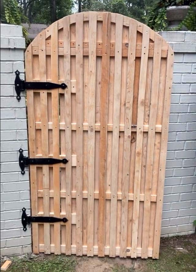 close look at brand new custom built cedar wood arched gate with black iron t hinges mounted on white brick fencing near Cooper Young District in Memphis, Tennessee by 1 Handy Craftsman